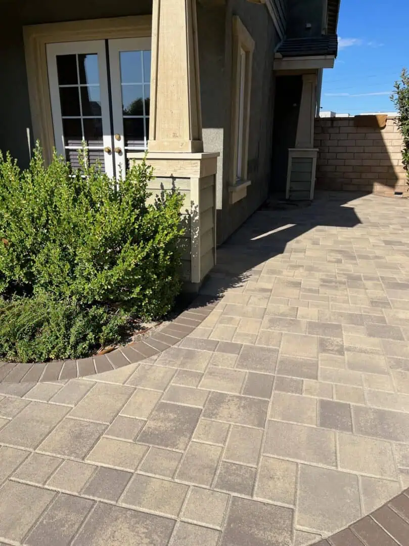A brick patio with bushes and a building.