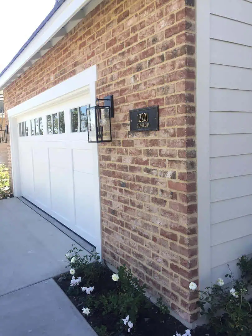 A white garage door and brick wall with flowers in the front.