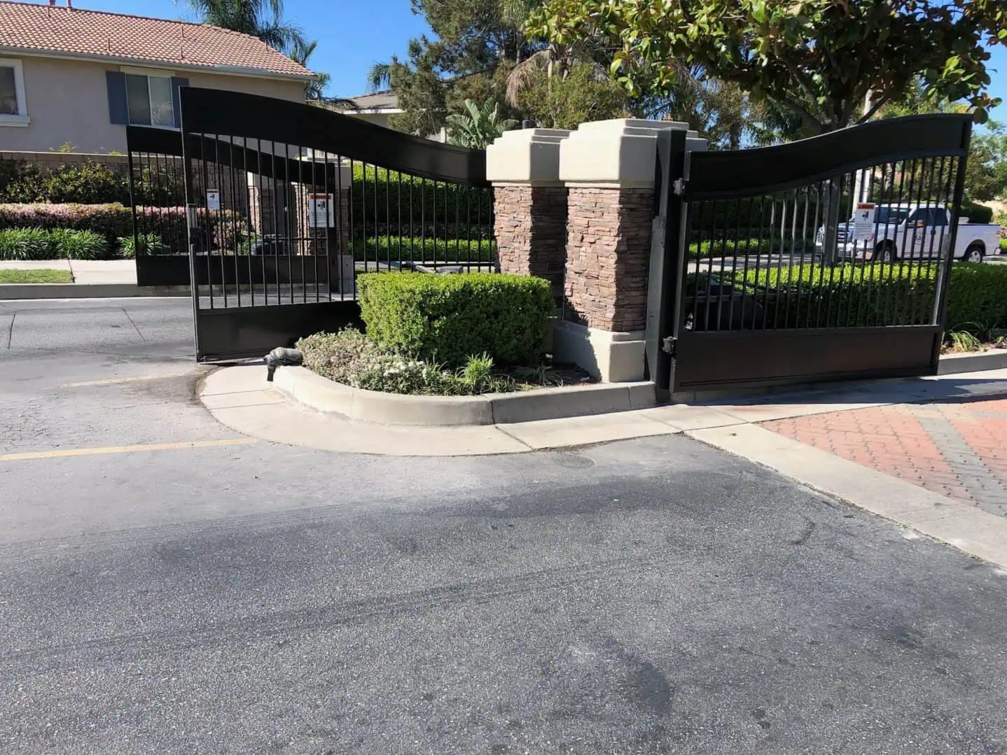 A gated driveway with a brick pillar and iron fence.