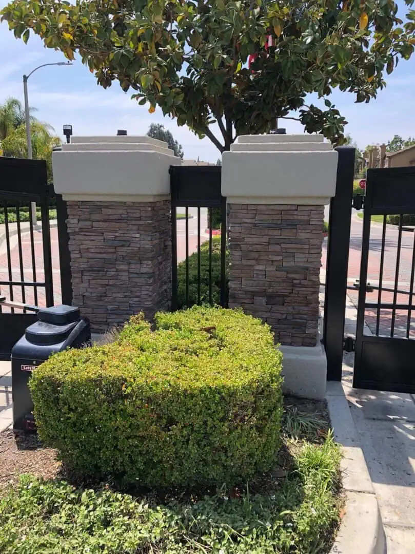 A hedge and bushes in front of two stone pillars.
