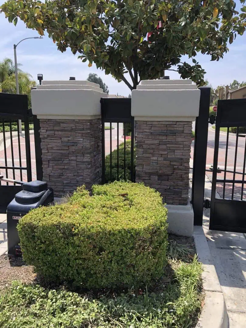 A hedge with two pillars and bushes in front of it