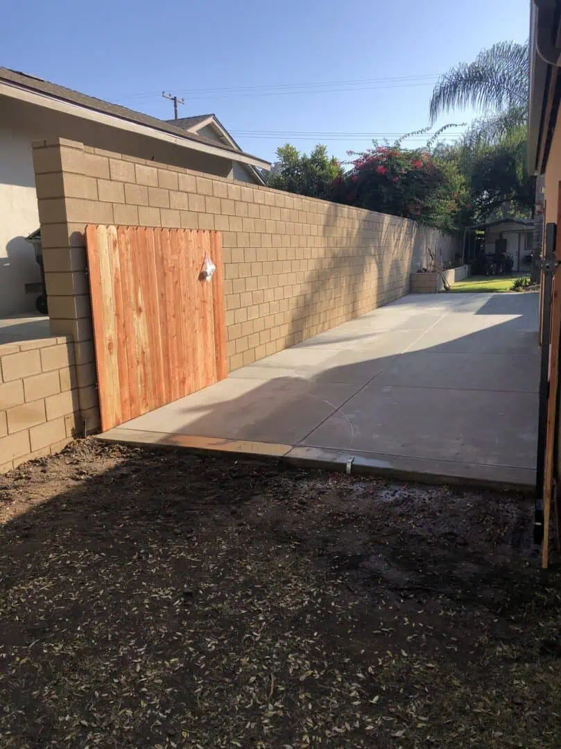 A driveway with a wooden gate and concrete wall.