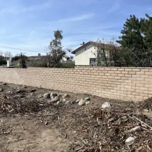 A newly built stone wall with houses and trees behind it under a blue sky.