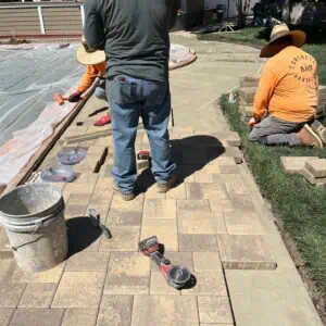 Workers installing outdoor pavers on a patio area.