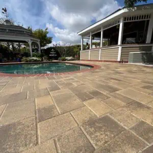 Spacious patio with stone tiles surrounding a clear swimming pool under a partly cloudy sky.