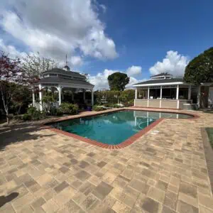 A backyard pool area with a clear blue pool and surrounding patio under a partly cloudy sky.